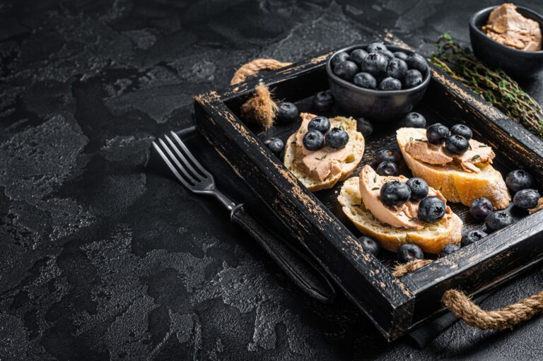 Foie gras toasts, duck liver pate and fresh blueberry in wooden tray. Black background.