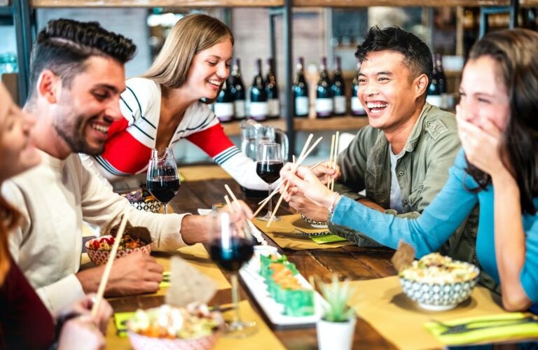 Multicultural trendy friends eating sushi with chopsticks at fusion restaurant bar